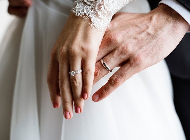 ľavé ruky nevesty a ženícha so zásnubným prsteňom a obrúčkou na prstenníku