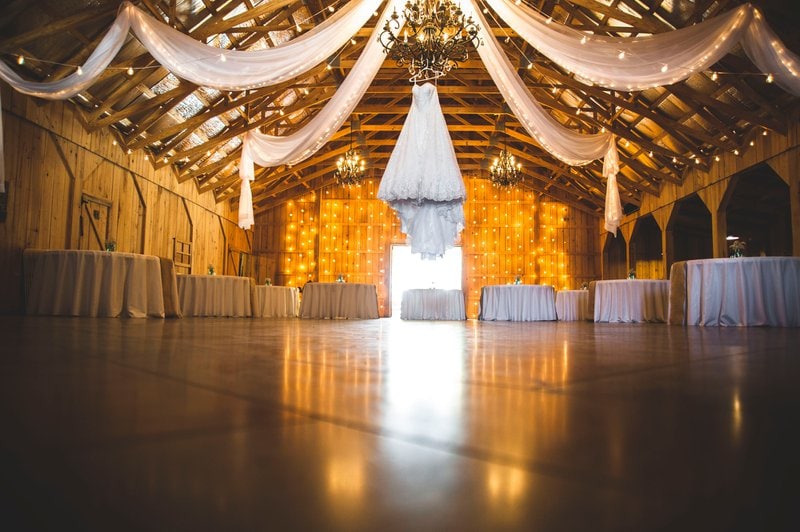 stodola vyzdobená bielymi stuhami a ozdobenými stolmi pripravená na svadobnú hostinu