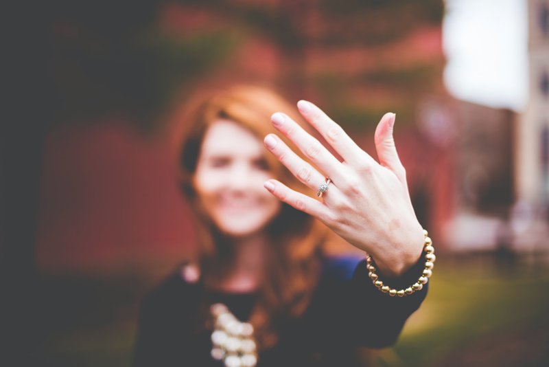 žena s ryšavými vlasmi ukazuje ľavú ruku s detailom na zásnubný prsteň