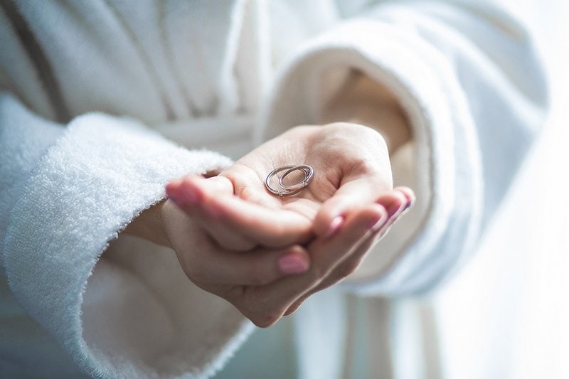 žena v župane drží v rukách diamantový zásnubný prsteň a obrúčku