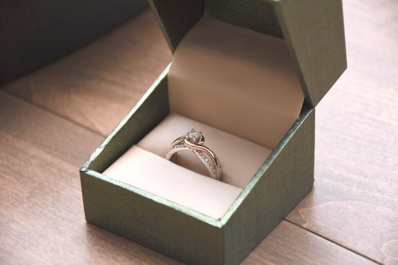 zlatý zásnubný prsteň s veľkým diamantom uprostred a malými postrannými diamantmi v šedej darčekovej krabičke