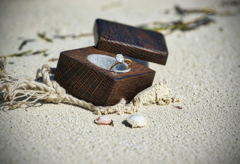 zásnubný diamantový prsteň uložený v drevenej krabičke na piesku