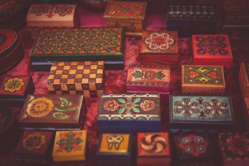 ozdobne dekorované farebné drevené šperkovnice zoradené v piatich radoch na červenej látke