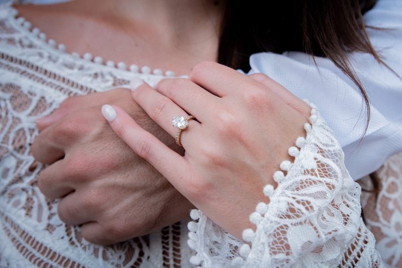 mužská ruka objímajúca ženu a žena s diamantovým prsteňom na prstenníku drží túto ruku