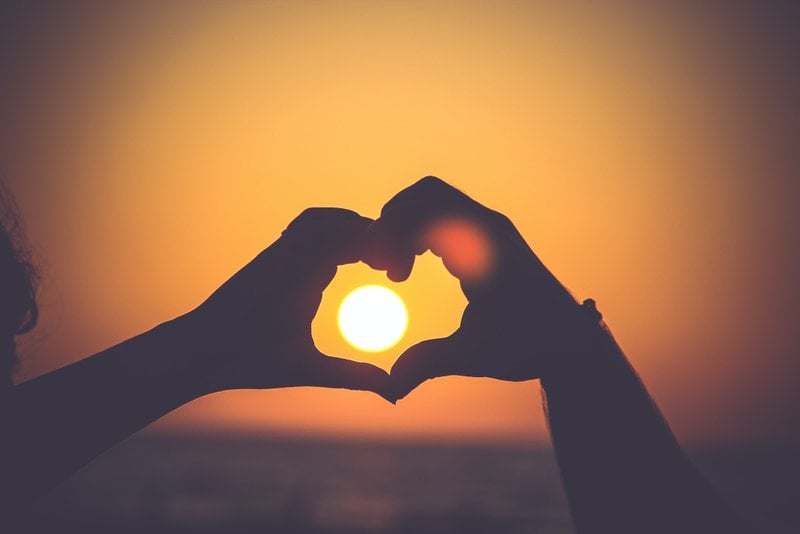 západ slnka cez ruky dvoch zamilovaných ľudí spojených do tvaru srdca