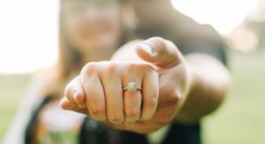 muž objíma žena zozadu držiac jej ruku s detailom na diamantový zásnubný prsteň