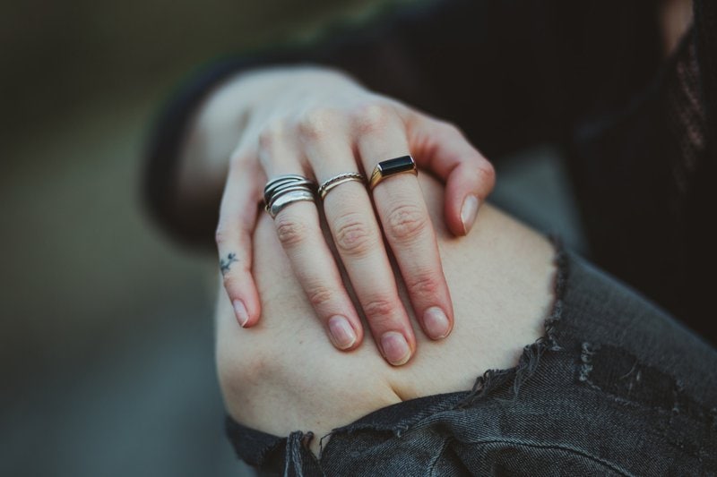 žena s prsteňmi na ruke dotýkajúca sa svojho odhaleného kolena v roztrhaných nohaviciach