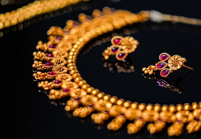 zlatý náhrdelník s náušnicami s ružovými drahokamami položené na čiernom pozadí
