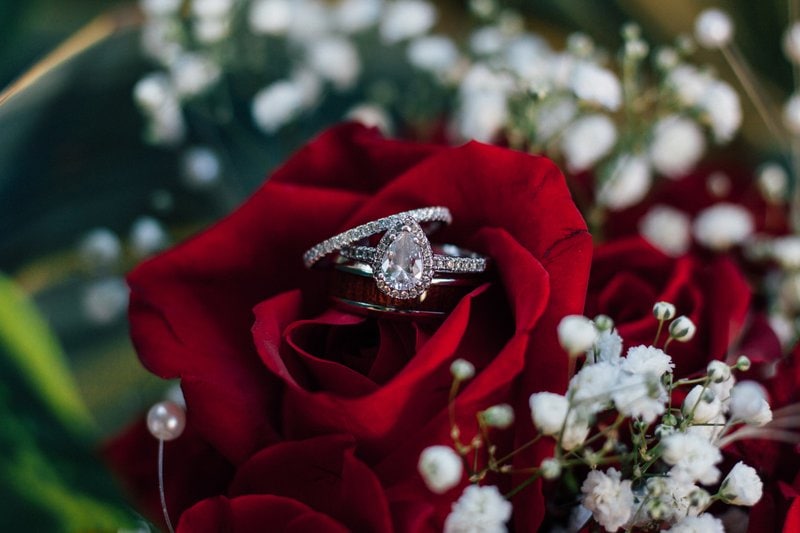 diamantový prsteň položený na kytici z červených ruží lemovanej malými bielymi kvietkami