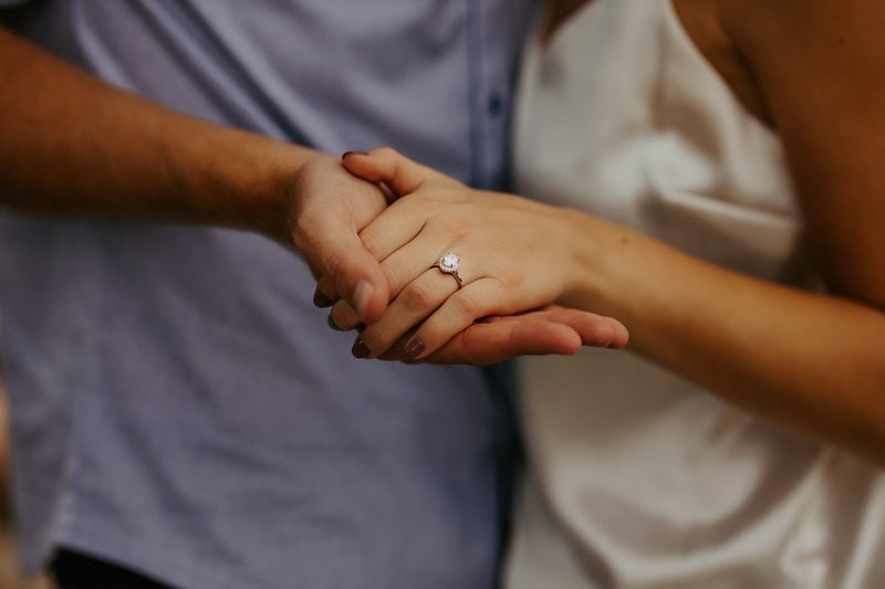 muž držiaci ženskú ruku s diamantovým prsteňom