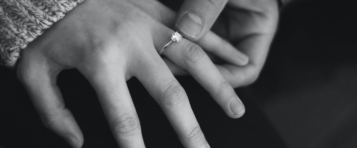 mužská ruka drží ženskú ruku so zásnubným prsteňom na prstenníku na čiernobielom pozadí