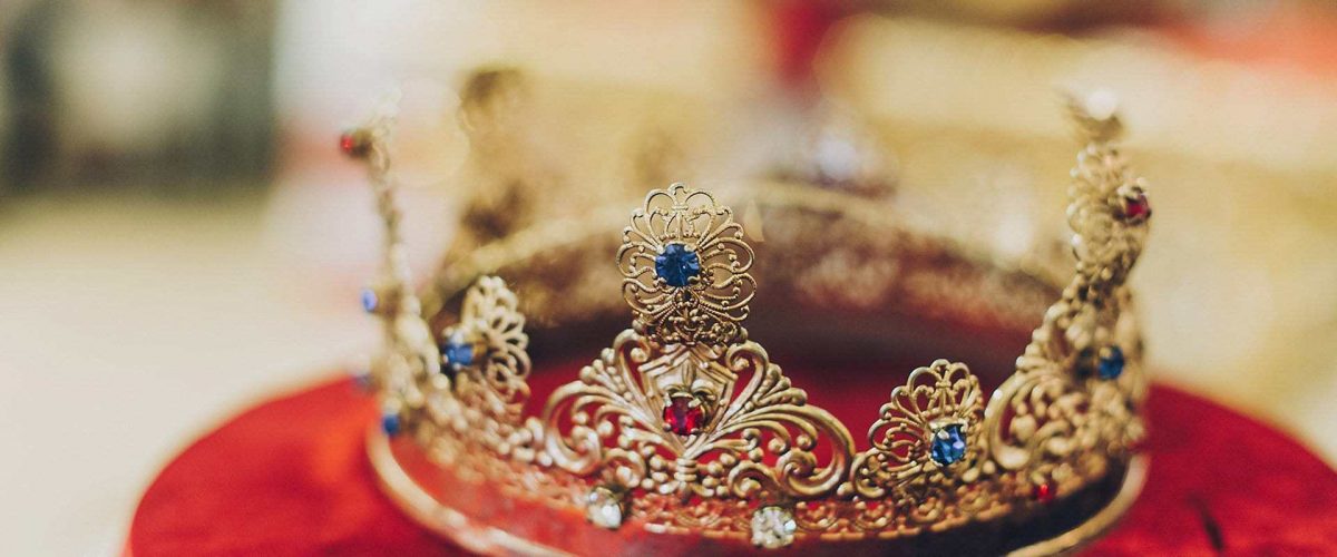 zlatá kráľovská koruna zdobená diamantmi na červenom zamatovom podklade
